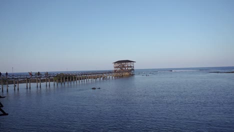 three surfers retreat from surfing area at the end of a long pier with a multi-level observation tower