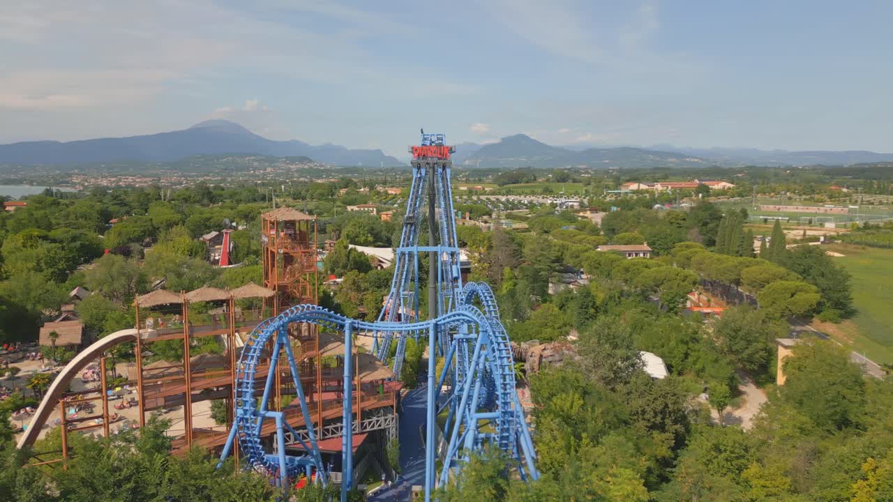 las sinuosas y retorcidas vías azules de una gran torre de montaña rusa sobre el parque de atracciones del lago de garda, italia