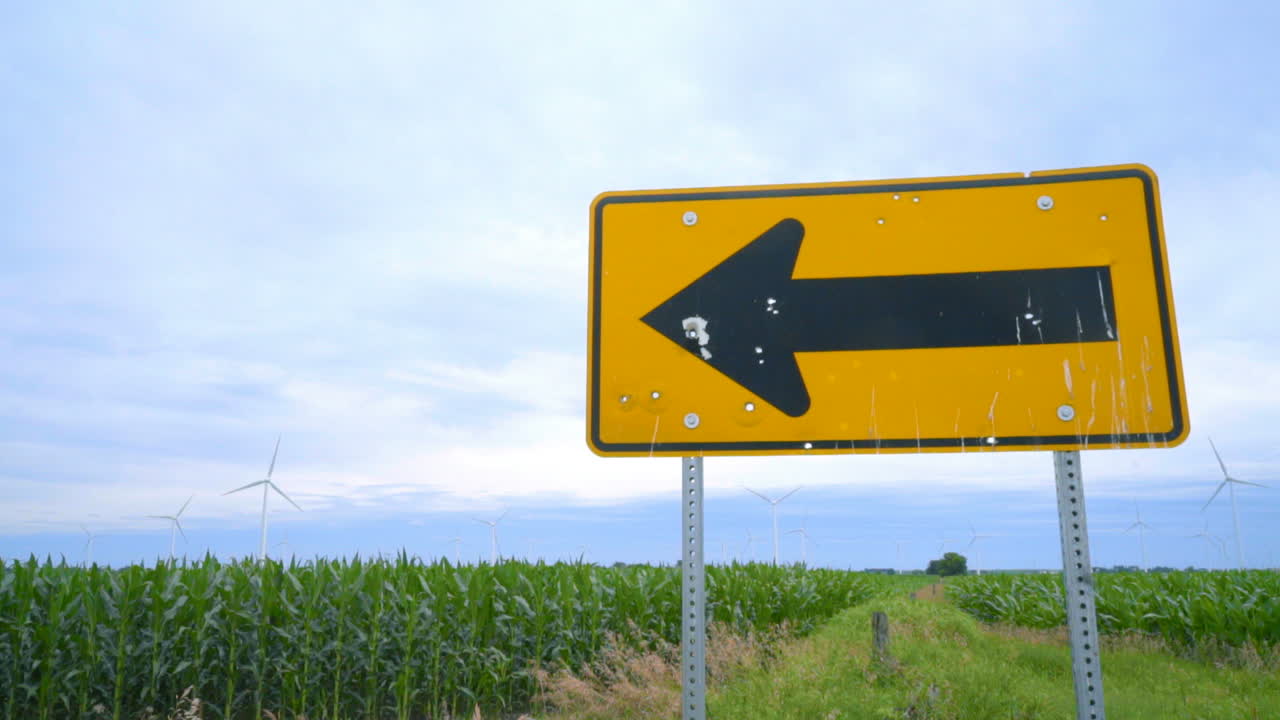 Road sign pointing to wing turbines farm. Farm field with wind turbines