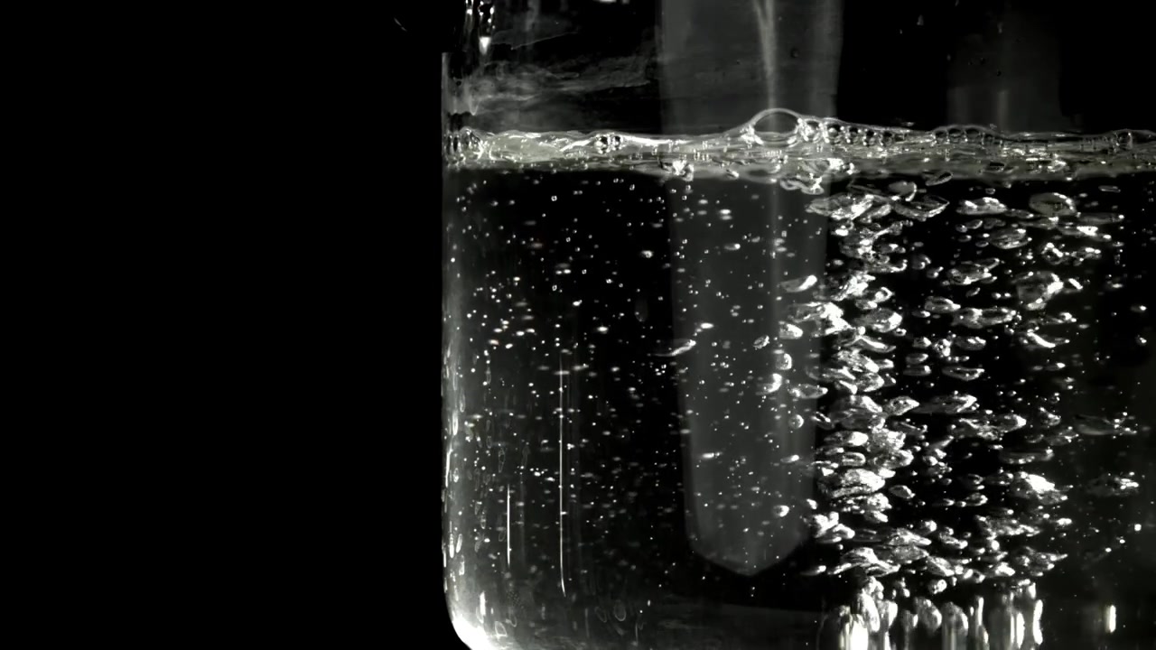 Bolle che salgono in acqua limpida in un bicchiere su sfondo nero
