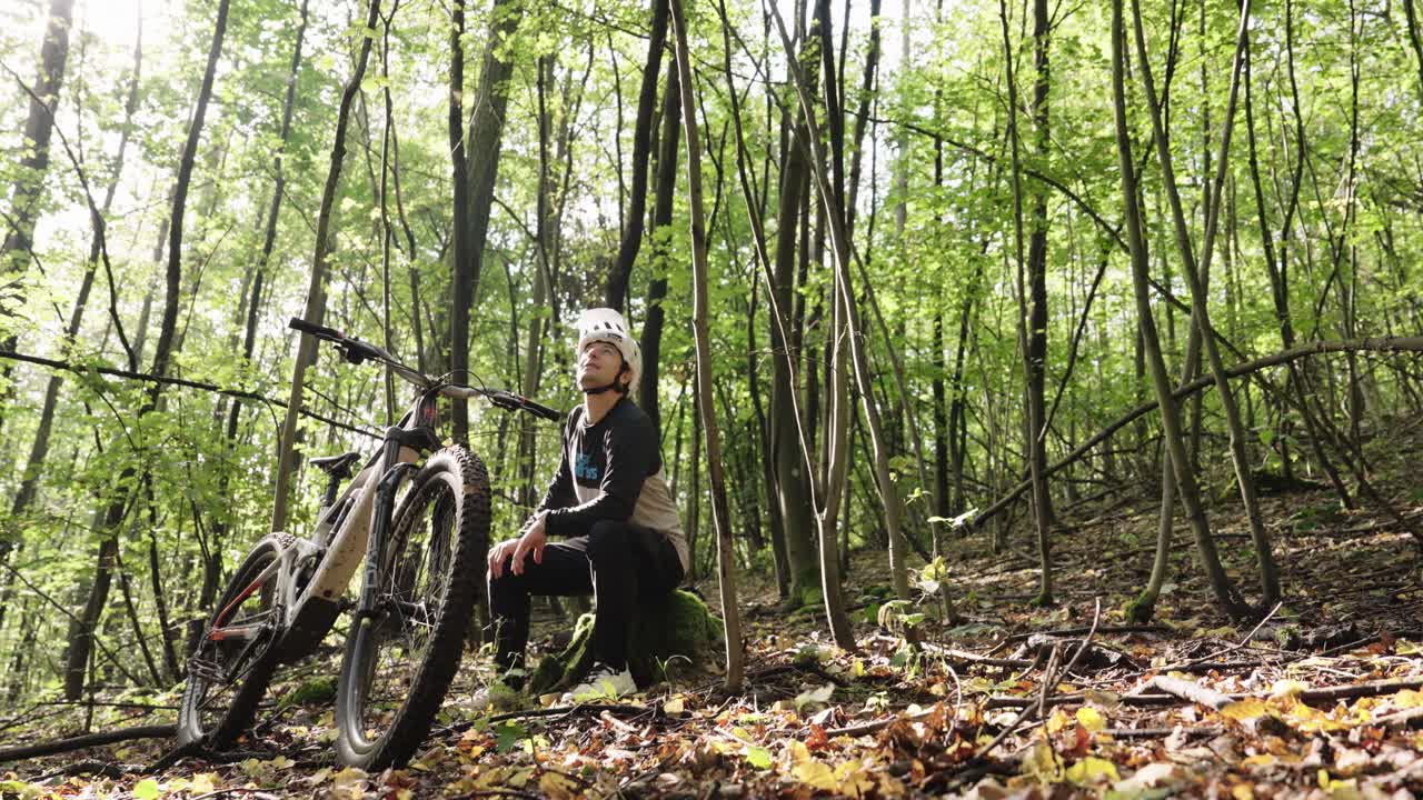 MTB athlete sit on tree stump and rest in green forest environment, Czechia