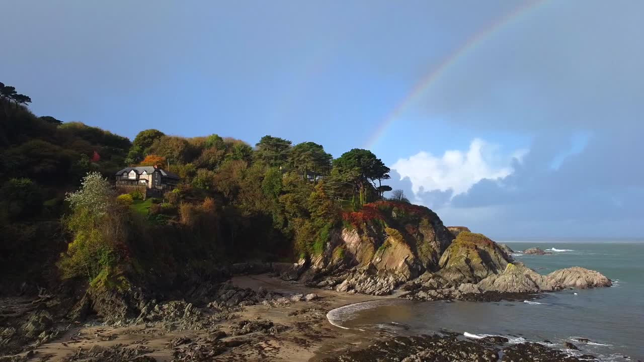 toma aérea de seguimiento de drones de una playa inglesa con acantilados rocosos y un arco iris en el fondo - lee bay, beach, ilfracombe, devon