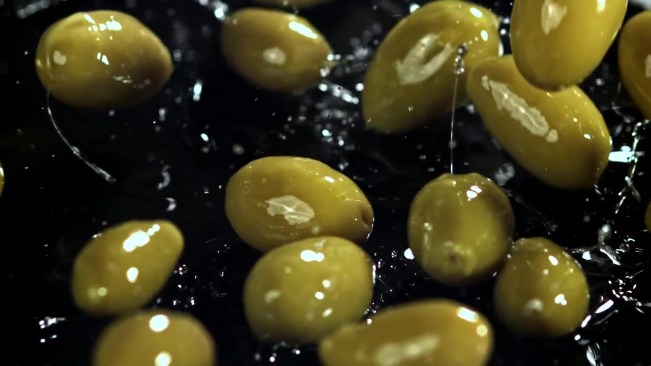 Olive verdi che cadono e schizzano su sfondo nero al rallentatore