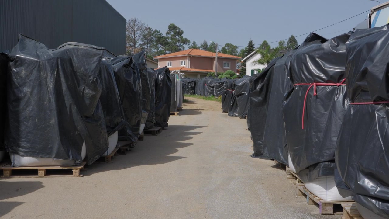 File di pallet avvolti in teli di plastica nera, immagazzinati all'aperto nel cortile di una fabbrica