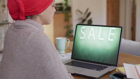 Biracial-woman-at-table-using-laptop,-online-shopping-during-sale,-slow-motion