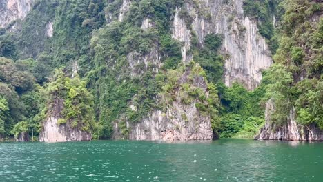 Boating-on-Khao-Sok-Lake,-Thailand,-reveals-foreground-rocks-with-lush-vegetation-emerging-from-the-water