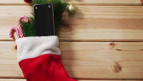 Video-of-christmas-decorations-with-smartphone-in-stocking-copy-space-on-wooden-background
