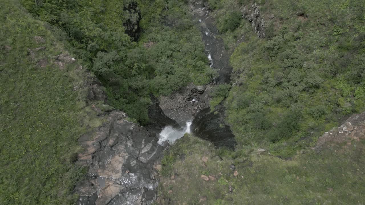 inclinación aérea sobre el borde de una cascada alta y pequeña en un valle verde y exuberante