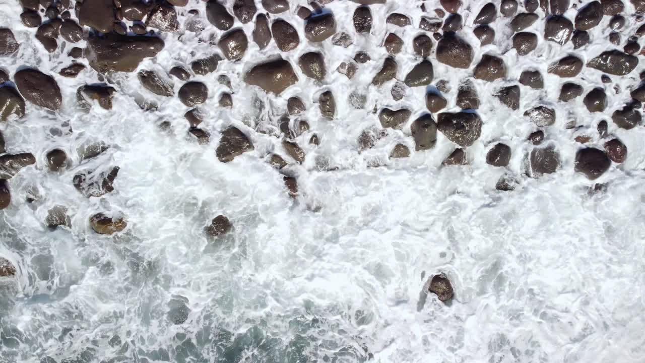 Top down background view of waves foam splashing on pebbles rock coast, Tenerife