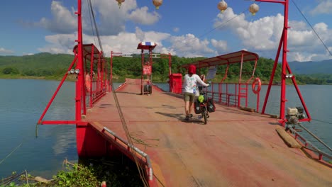 Following-shot-of-a-female-cyclist-walking-over-metal-barge-on-lake-in-Pak-Nai-fisherman-village,-Nan-province,-Thailand-on-a-sunny-day