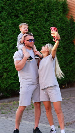woman takes selfie of her family standing outdoors. taking photos of a happy parents and son. vertical video