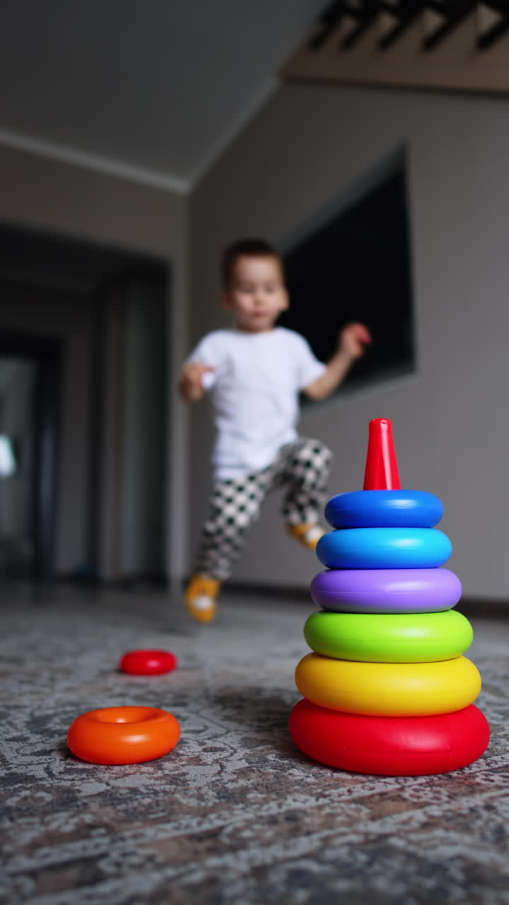 Baby boy runs into the room near the toy pyramid. Cute kid starts to assemble the toy. Vertical video.