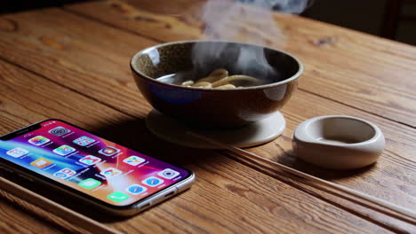 wooden table with hot noodles, phone and chopsticks