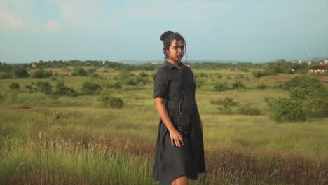 young woman in a black dress in a meadow landscape, looking directly into the camera