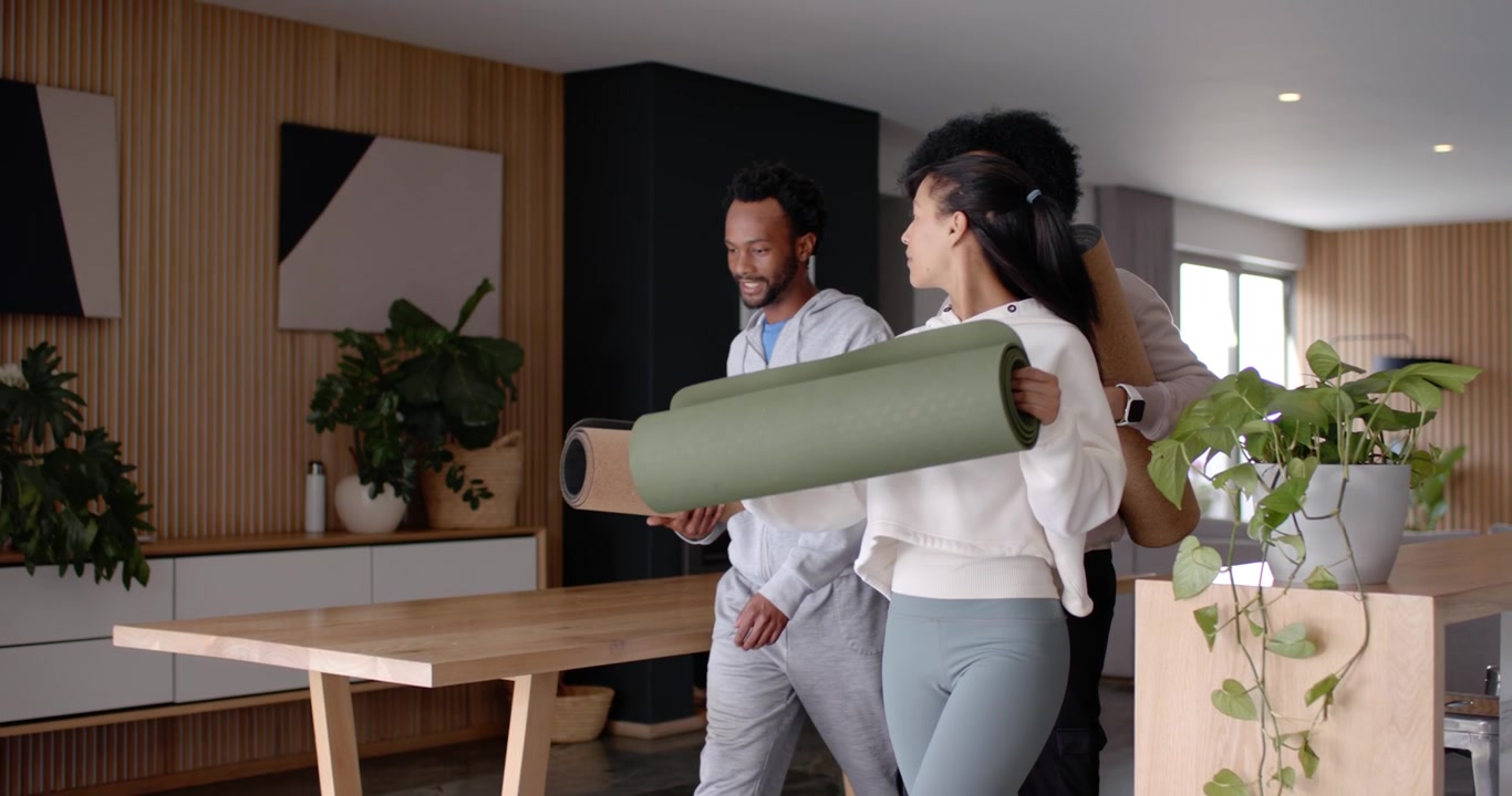 Amigos afro-americanos entrando na cozinha segurando tapetes verdes escuros e um tubo, preparando-se para yoga