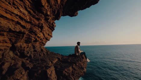 man sitting on a cliff overlooking the ocean