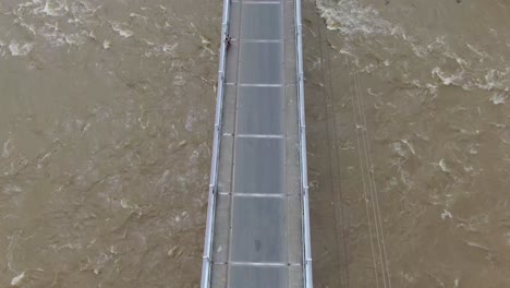 vista de arriba hacia abajo del puente colgante con el río marrón corriendo y las rocas dentadas
