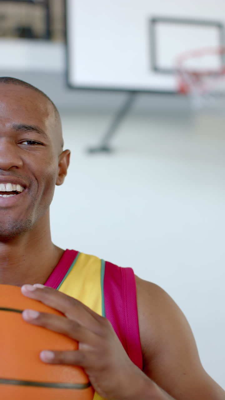 Vertical video: Holding basketball, smiling man in sports jersey standing in indoor court