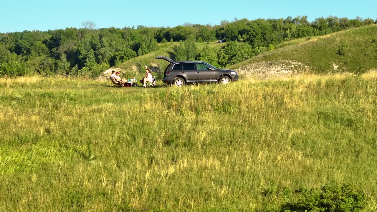 한 커플 이 언덕 꼭대기 에 있는 차 를 타고 피크닉 을 즐기고 있다