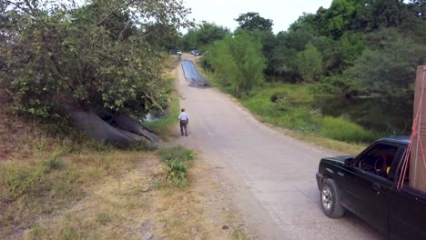 Shot-of-a-man-walking-on-a-long-road-in-the-countryside-as-a-pickup-truck-carrying-appliances-drives-past-him