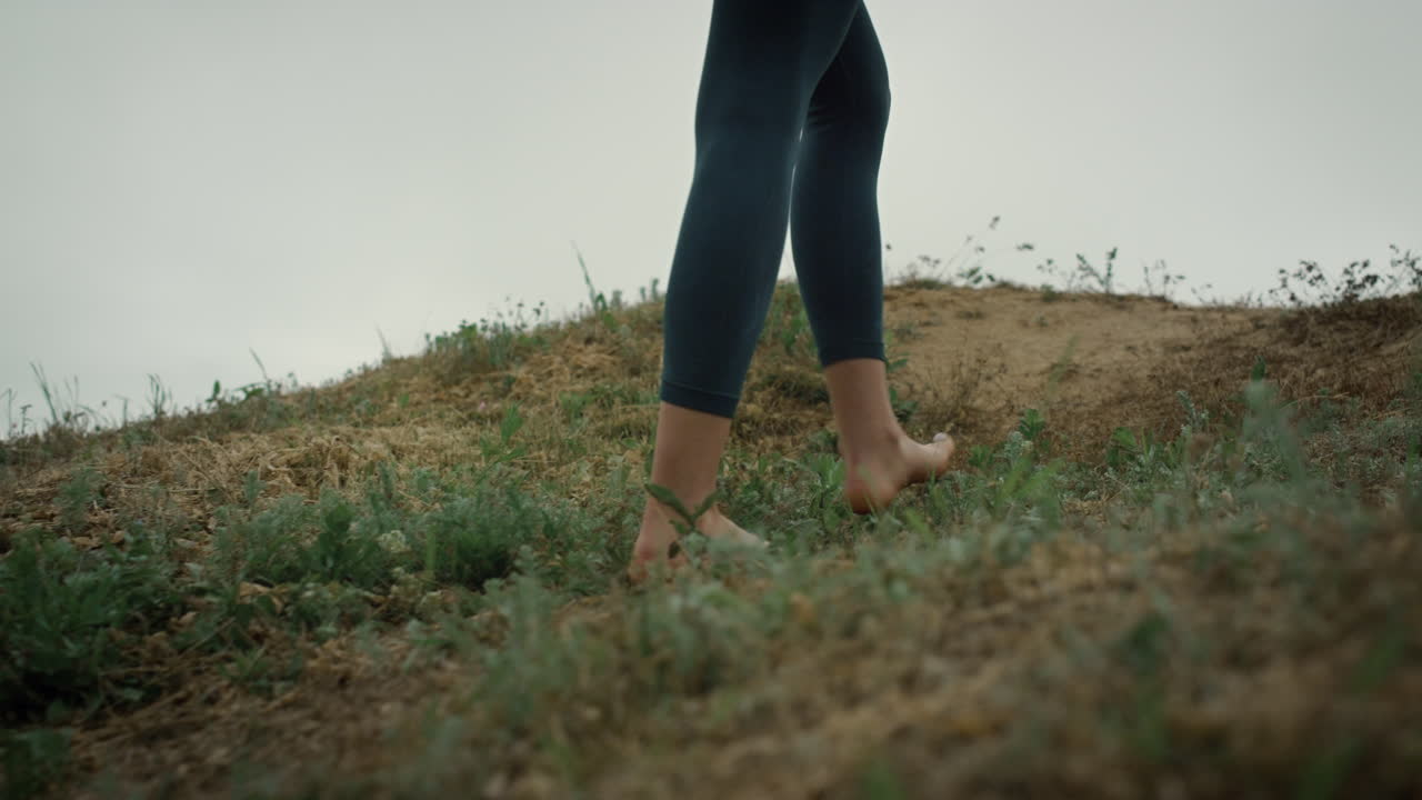 Barefoot girl climbing green hill close up. Young lady feet walking seacoast.
