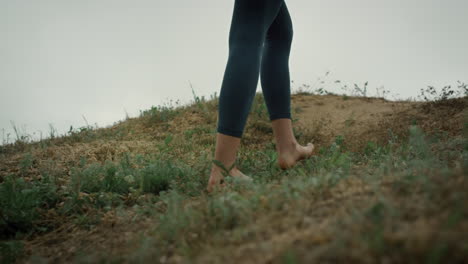 Barefoot-girl-climbing-green-hill-close-up.-Young-lady-feet-walking-seacoast.
