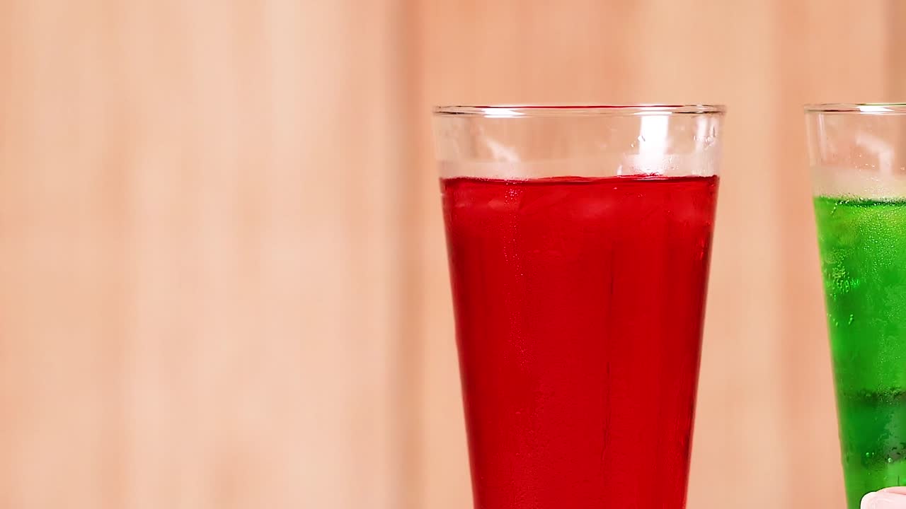 Close-up of red and green beverages in tall glasses against a wooden backdrop.