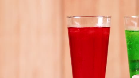 close-up of red and green beverages in tall glasses against a wooden backdrop.