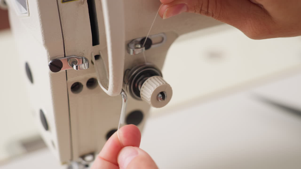 Female hand gently fixing yarn thread on tension control of sewing machine, emphasizing precise adjustment, mechanical detail, and steady positioning in neat workspace, ensuring proper stitch quality