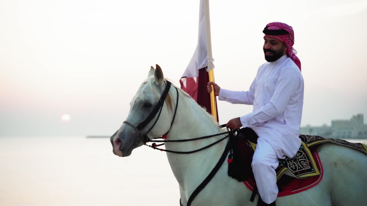 un caballero montando un caballo sosteniendo la bandera de qatar cerca del mar