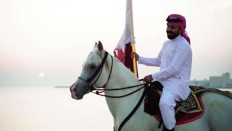 a knight riding a horse holding qatar flag near the sea