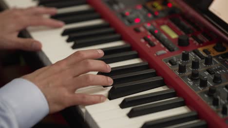 close up of a musician’s hands playing a red digital keyboard with illuminated controls
