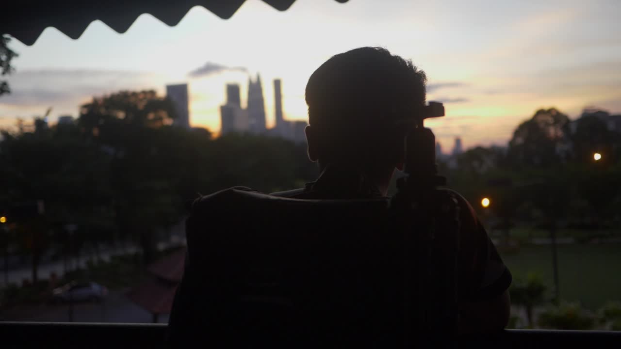 [랙 포커스] 해가 지는 동안 쿠알라  ⁇ 푸르 도시 스카이라인을 내려다보는 남자의 실루 ⁇  팬  ⁇