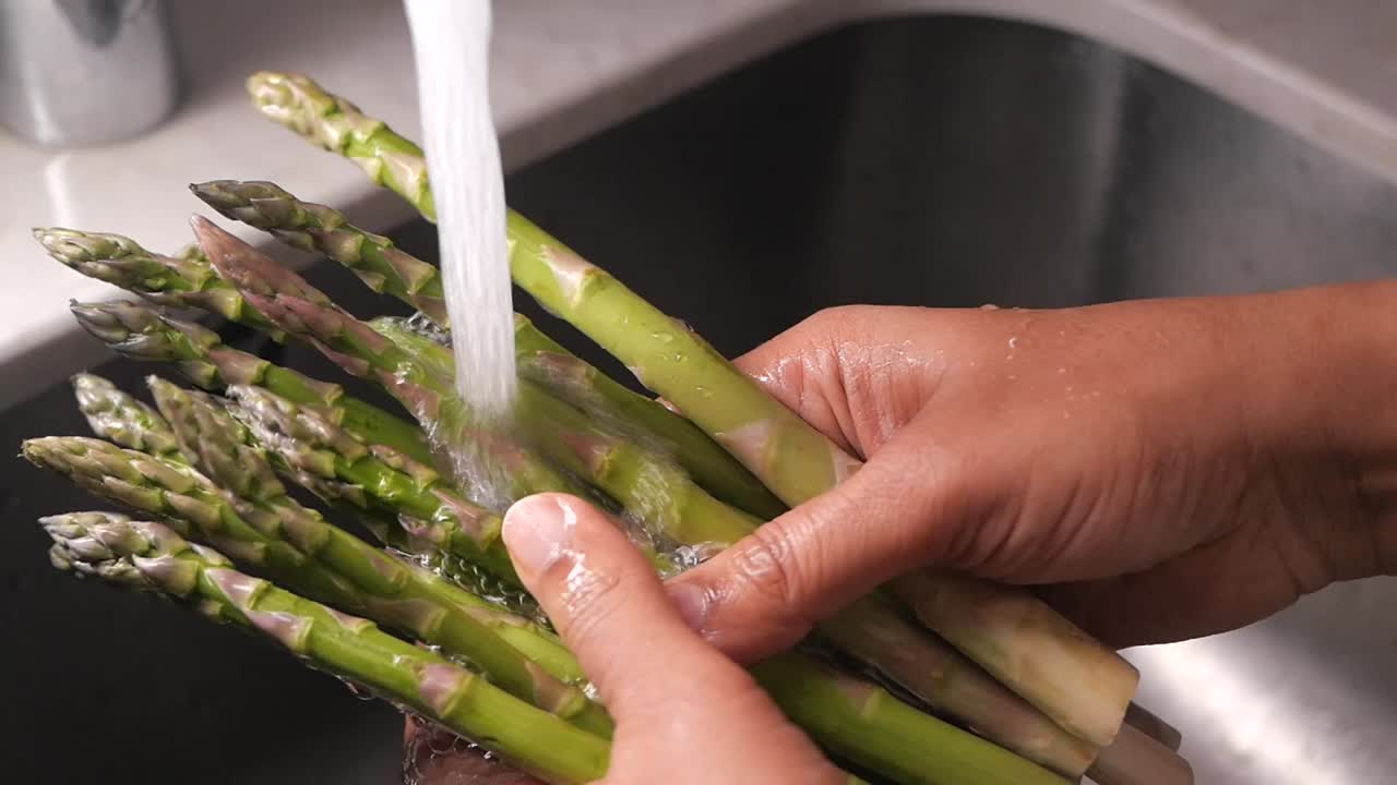 Mani che lavano asparagi verdi freschi sotto acqua corrente nel lavello della cucina