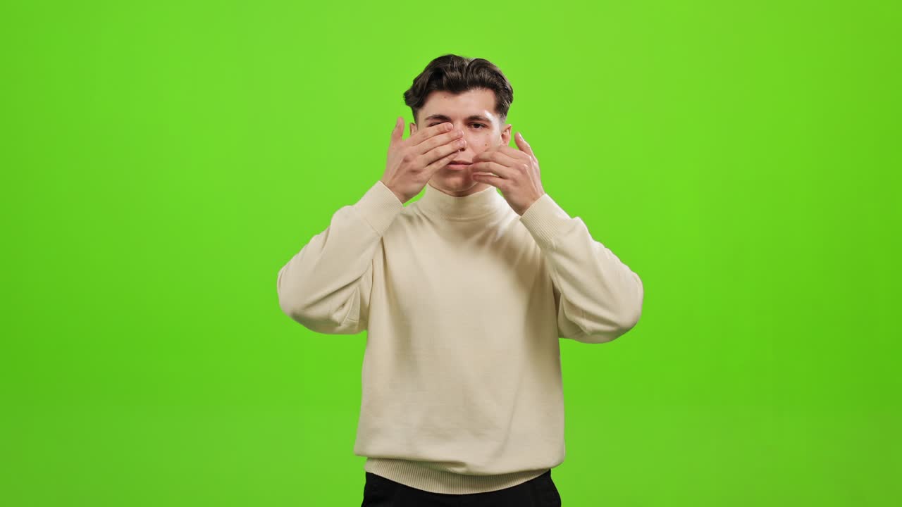 мужчина стоит и смотрит в камеру. он закрывает уши, рот и глаза руками. он стоит на зеленом фоне. зеленый экран. 4k.