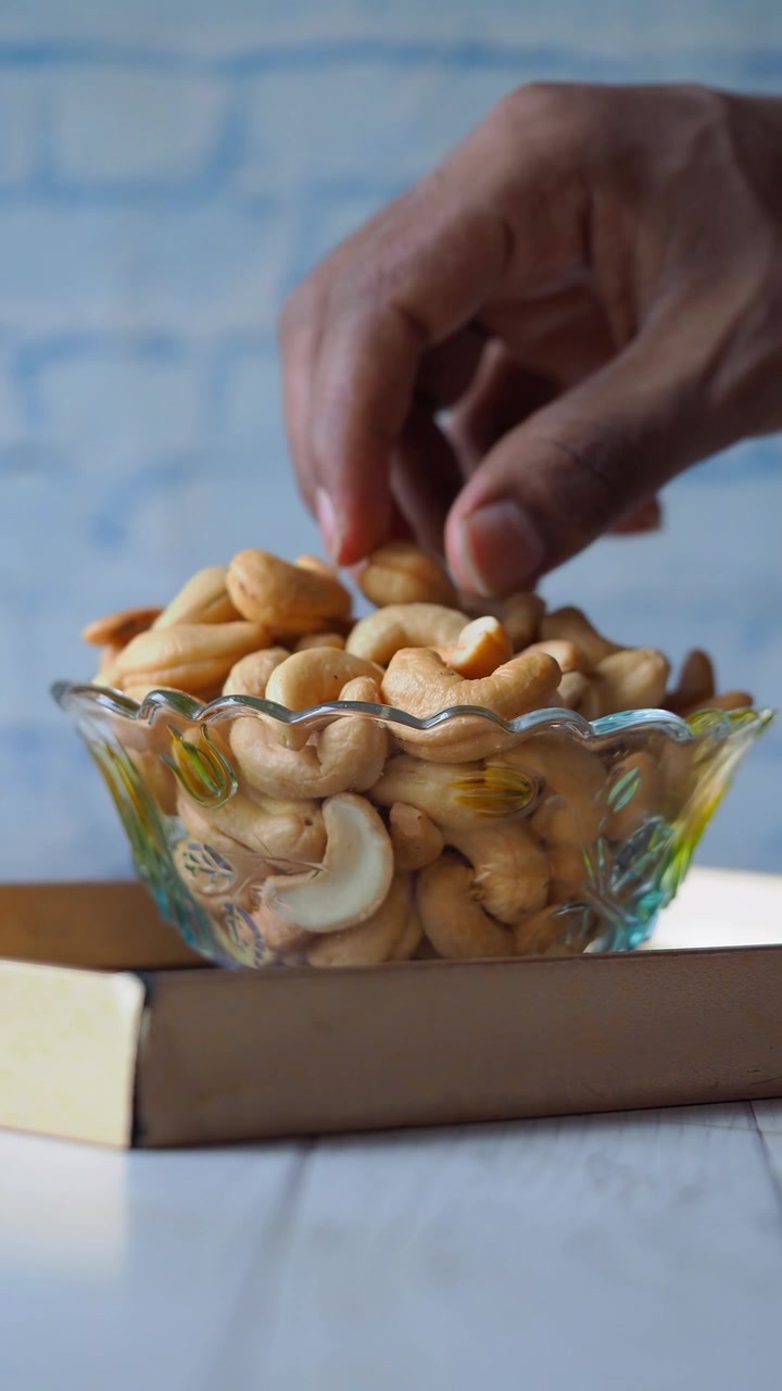 Hand Picking Roasted Cashew Nuts from a Glass Bowl
