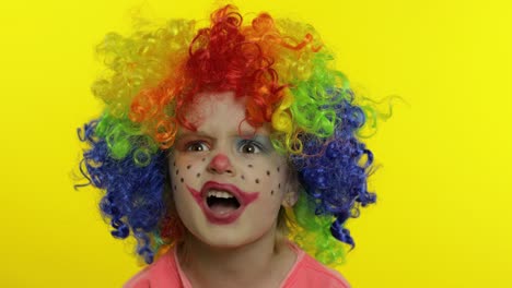 Little-child-girl-clown-in-rainbow-wig-tells-something-interesting.-Having-fun,-smiling.-Halloween