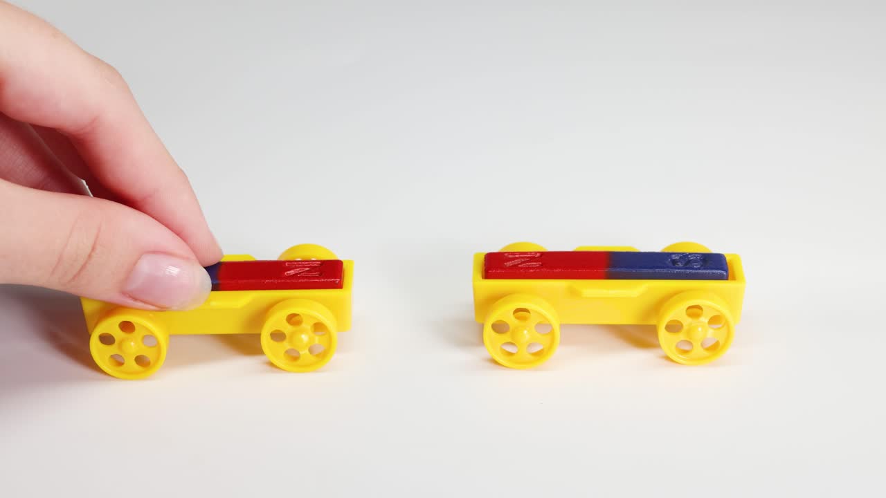Hands manipulate colorful toy cars with magnets, illustrating magnetic attraction and repulsion on a white surface