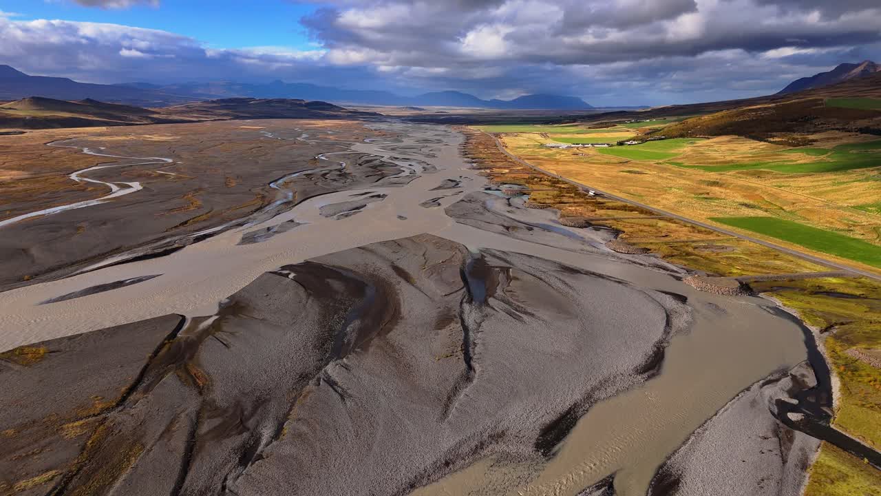 Icelandic streams twist like veins on their journey through glaciated volcanic valleys, rock and vibrant green farmed flatlands to the sea. Drone aerial fly through to horizon