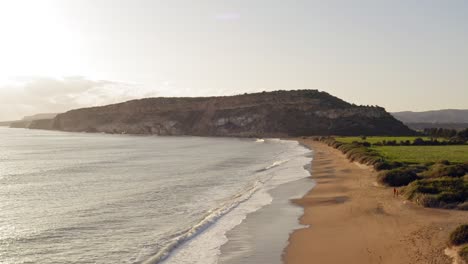 cinematic drone shot flying above glorious beach approaching large hill as waves crash on the shore