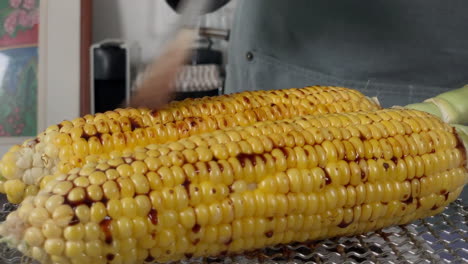 a japanese female chef puts shoyu on grilled corn at her home kitchen, tokyo, japan