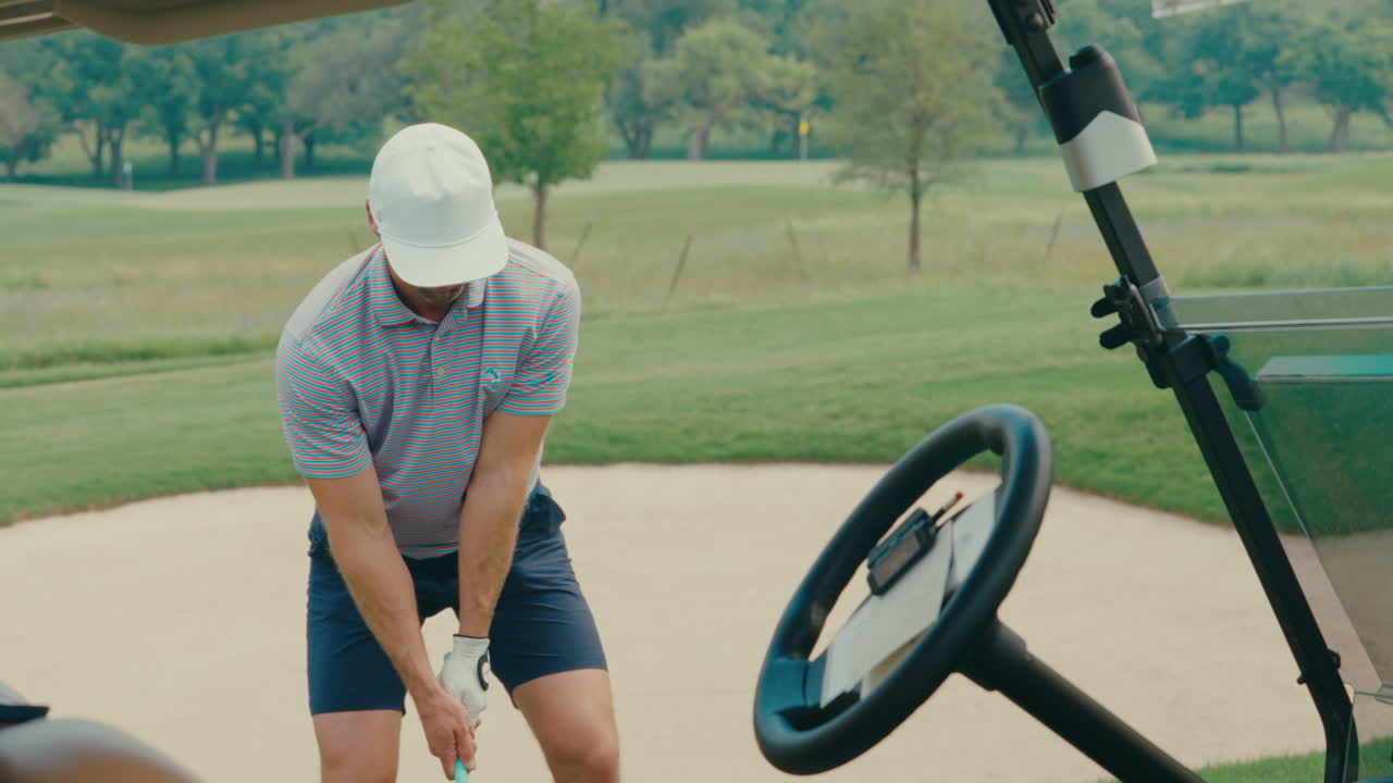 A male golfer hits an iron off the fairway in slow motion. The shot is framed from a partner POV angle through a golf cart, creating a unique, immersive view of the swing and impact.