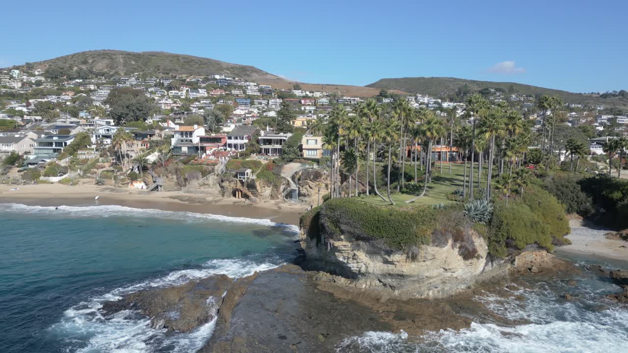 4K drone shot flying around palm trees along the ocean at Laguna Beach during daytime. Slow motion capable, ideal for travel, tropical, coastal, or cinematic projects