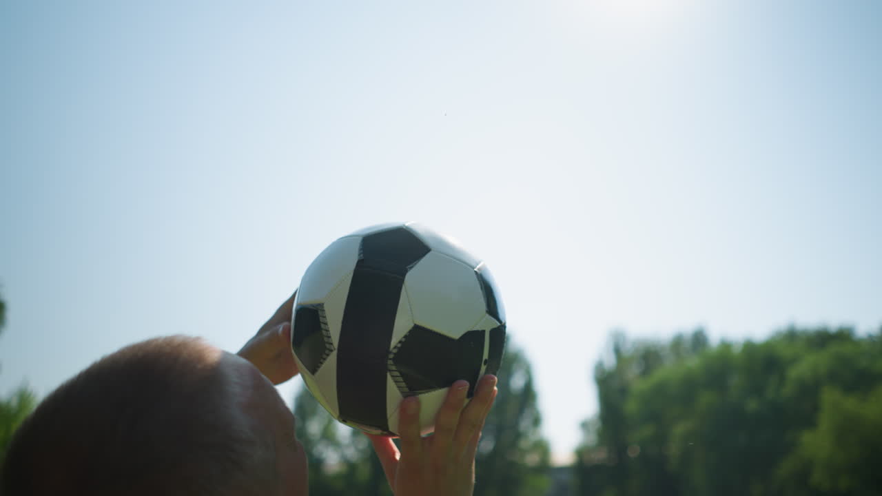 Close-up of a middle-aged man skillfully rotating a soccer ball in the air and catches it back, with blurred trees in the background and a clear sky