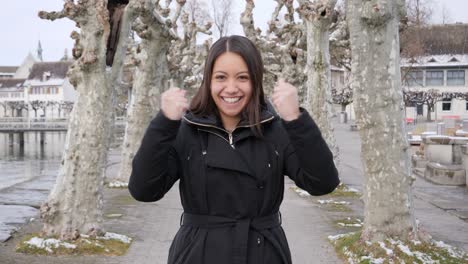 Young-attractive-woman-raises-her-arms-and-cheers-a-success-while-standing-in-wintry-city-landscape