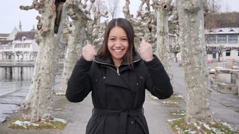 young attractive woman raises her arms and cheers a success while standing in wintry city landscape