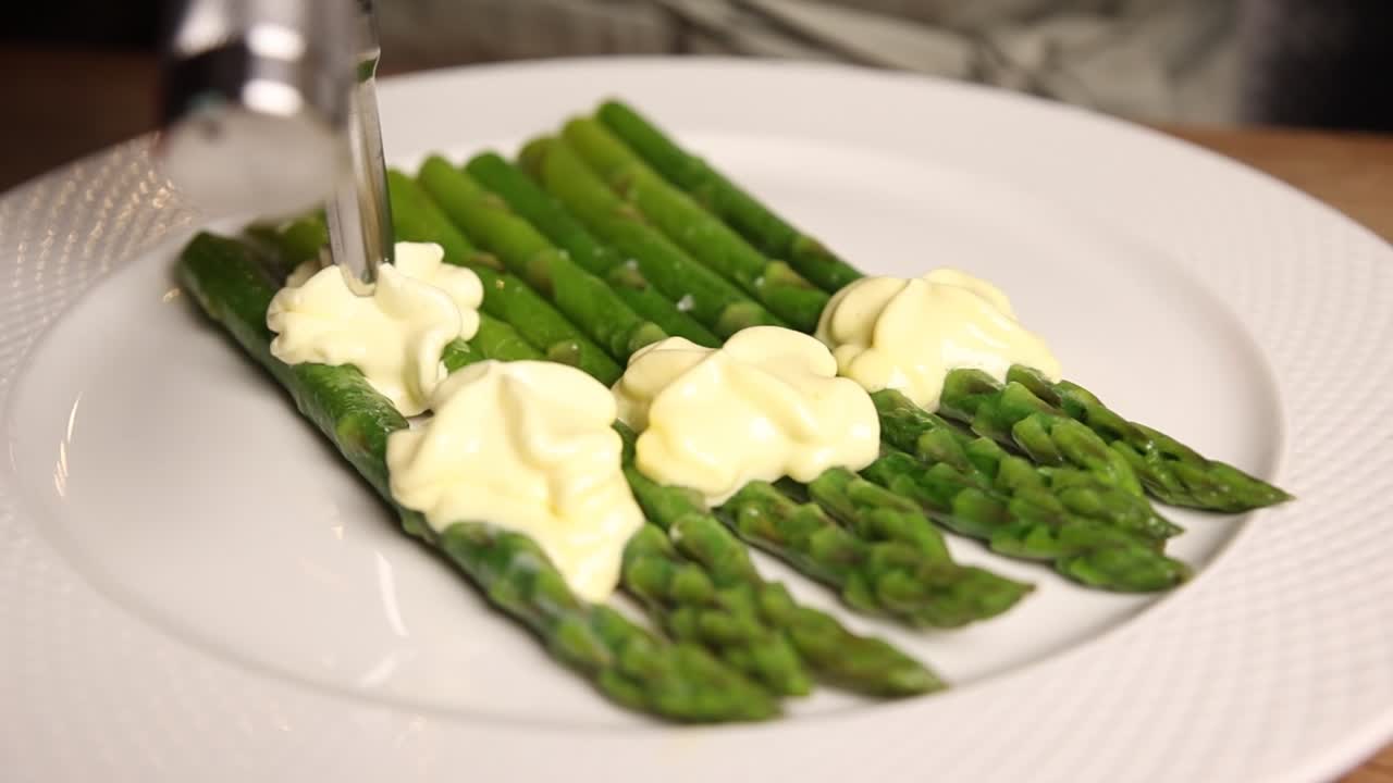 Dresser de la mayonnaise sur des pointes d'asperges vertes fraîches, sur une assiette blanche