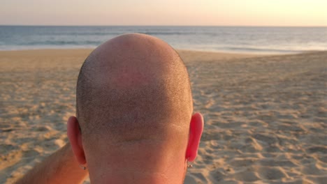 hombre caucásico en la playa toca su cabeza calva afeitada alopecia concepto de trasplante confiado