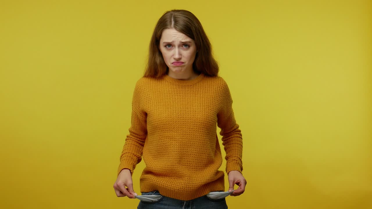 Frustrated upset poor girl with brown hair in pullover turning out pockets gesturing no money