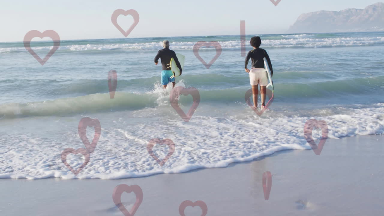 Running into ocean waves, two people with heart-shaped animation overlaying scene